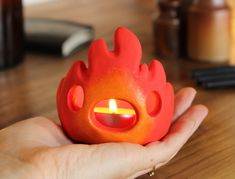 a hand holding an orange candle with a flame in it's center on a wooden table