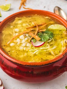 a red bowl filled with soup and garnished with cilantro, limes, onions, and other vegetables