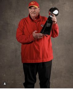 an older man in a red jacket holding up a trophy and looking at the camera