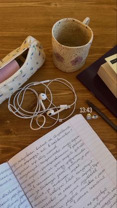 an open book, headphones and notebook on a wooden table next to a pair of earbuds