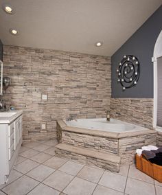 a large bathroom with a stone wall and tub in the corner, along with white cabinets