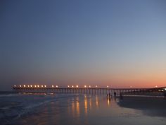 people are walking on the beach at night with lights in the sky over the water