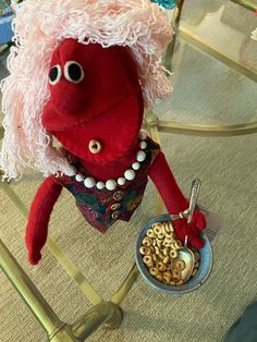 a red stuffed animal holding a bowl of cereal on top of a glass table with other items