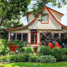 a white house with red trim sitting in the middle of a lush green yard next to trees