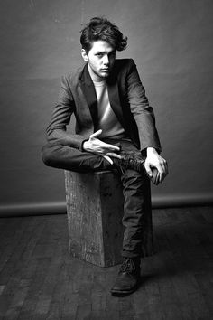 black and white photograph of a man sitting on a wooden block in front of a wall