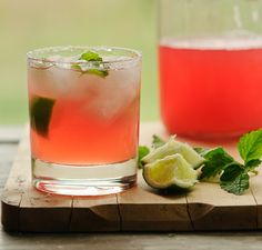 two glasses filled with drinks sitting on top of a wooden cutting board