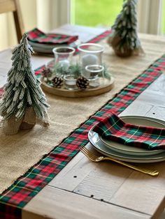 the table is set for christmas dinner with plaid napkins and pine trees on it