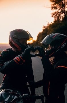 two people wearing helmets are sitting on a motorbike in the street at sunset