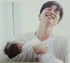 a man holding a baby in his arms and smiling at the camera while wearing a white shirt