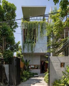 the house is surrounded by greenery and concrete walls, with an iron gate leading to it