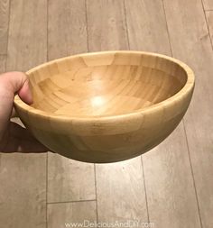 a hand holding a wooden bowl on top of a tile floor next to a wood floor