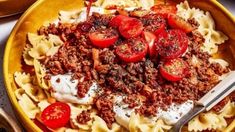 a yellow bowl filled with pasta and meat covered in sauce, tomatoes and sour cream