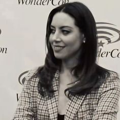 a woman sitting at a table in front of a wall with wonder con logo on it