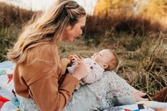 a woman holding a baby while sitting on a blanket