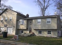 a two story house with green grass and trees in the background