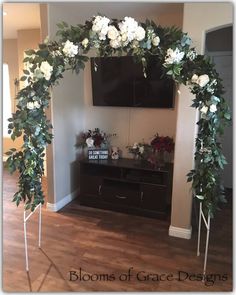 an arch with white flowers and greenery on it in front of a television screen