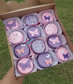 a box filled with lots of purple cupcakes on top of a green field