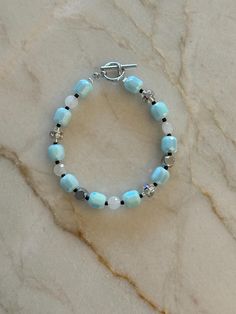 a blue bracelet with white beads and silver accents on a marble slabd countertop