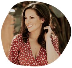 a woman in a red and white floral shirt smiles at the camera with her hand on her ear