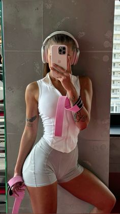 a woman in white and pink is taking a selfie with her cell phone while wearing headphones