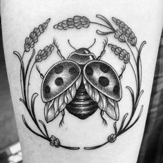 a ladybug tattoo on the leg with flowers and leaves around it, in black and white