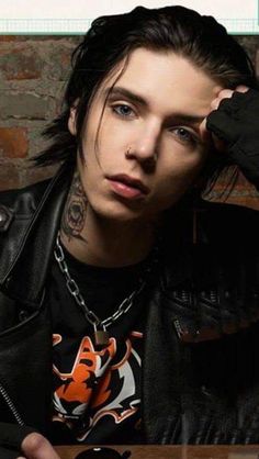 a man with long hair and piercings sitting at a table in front of a brick wall