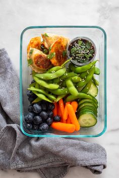 a plastic container filled with vegetables and meats next to a gray napkin on top of a white counter