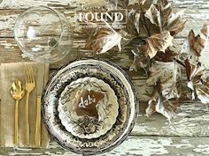 the table is set with plates, silverware and autumn leaves