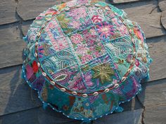 a colorful patchwork round pillow sitting on top of a wooden floor next to a brick wall