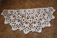 white crocheted doily sitting on the floor next to a brown carpeted area