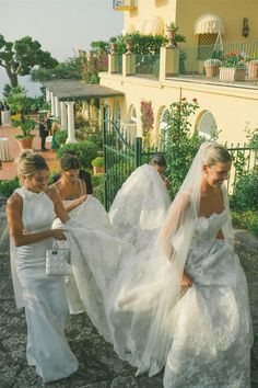 three women in white dresses are walking down the street with veils over their heads