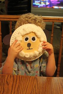 a young boy holding up a paper plate with a sheep face on it