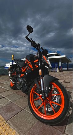 an orange and black motorcycle is parked on the sidewalk