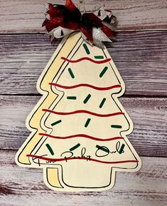 a wooden christmas tree ornament hanging on a wood wall with red and green ribbon