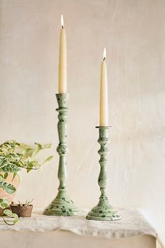 two candles are sitting on a table next to a potted plant and a candle holder