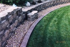 a stone wall next to a green lawn