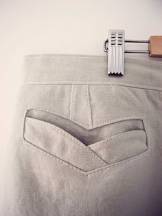 a pair of grey pants hanging on a white wall next to a wooden hanger