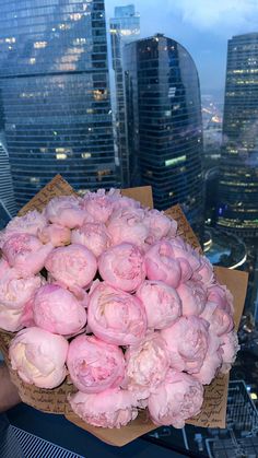 a bunch of pink flowers sitting on top of a cardboard box in front of a cityscape