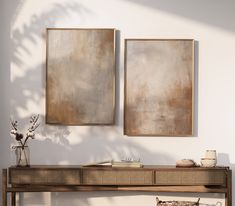 two paintings hang on the wall next to a console table with baskets and vases