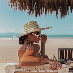 a woman sitting on top of a beach chair under a straw hut next to the ocean