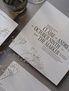 the wedding stationery is laid out on top of each other, with wine glasses in the background