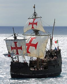 a large boat sailing across the ocean with people on it's back and red crosses on its sails