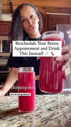 a woman holding up a jar filled with red liquid next to a glass full of water