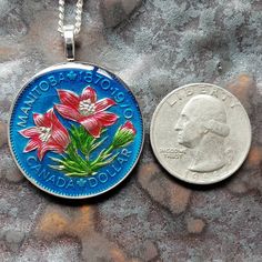 Coin Origin: Canada Features: Flowers. Manitoba 100 Years Size: Medium. 1-1/4 inch (32mm) Year: 1970 - only 1 year Metal type: Cupro-nickel This high quality coin jewelry was hand painted by Ann Nolen, owner of AnimalCoin of Santa Rosa, California. Perfect if you are shopping for a special gift or starting a collection of your own. Cherish a special place in the world, an animal or a piece of nature. AnimalCoin is special because Ann personally selects and hand paints each coin herself. No two a Artistic Handmade Crafts As Gifts, Handmade Artistic Crafts For Gifts, Artistic Handmade Crafts For Gifts, Blue Handmade Crafts For Gifts, Artistic One-of-a-kind Round Pendant Necklace, Collectible Engraved Coin-shaped Jewelry, Antique Coin-shaped Necklaces For Ceremonial Occasions, Cheap Antique Coin-shaped Necklaces, Antique Finish Coin-shaped Jewelry Gift