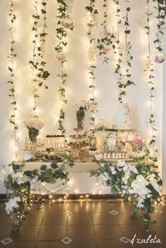 an image of a table with flowers on it and lights hanging from the wall behind it