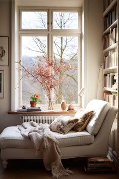 a white couch sitting in front of a window next to a book shelf filled with books