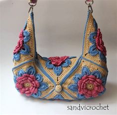 a crocheted purse with pink and blue flowers hanging from it's handle