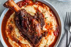 a white bowl filled with mashed potatoes topped with meat and garnished in sauce