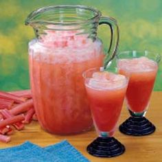 two glasses filled with liquid next to carrots and a pitcher full of watermelon juice