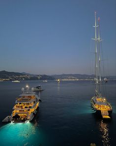 two boats in the water near each other with lights on them and some hills in the background